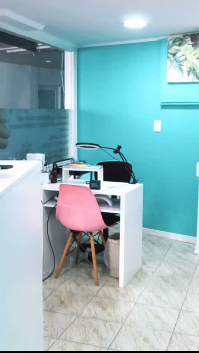 Mesa de manicuría con silla rosada contra la pared turquesa del local